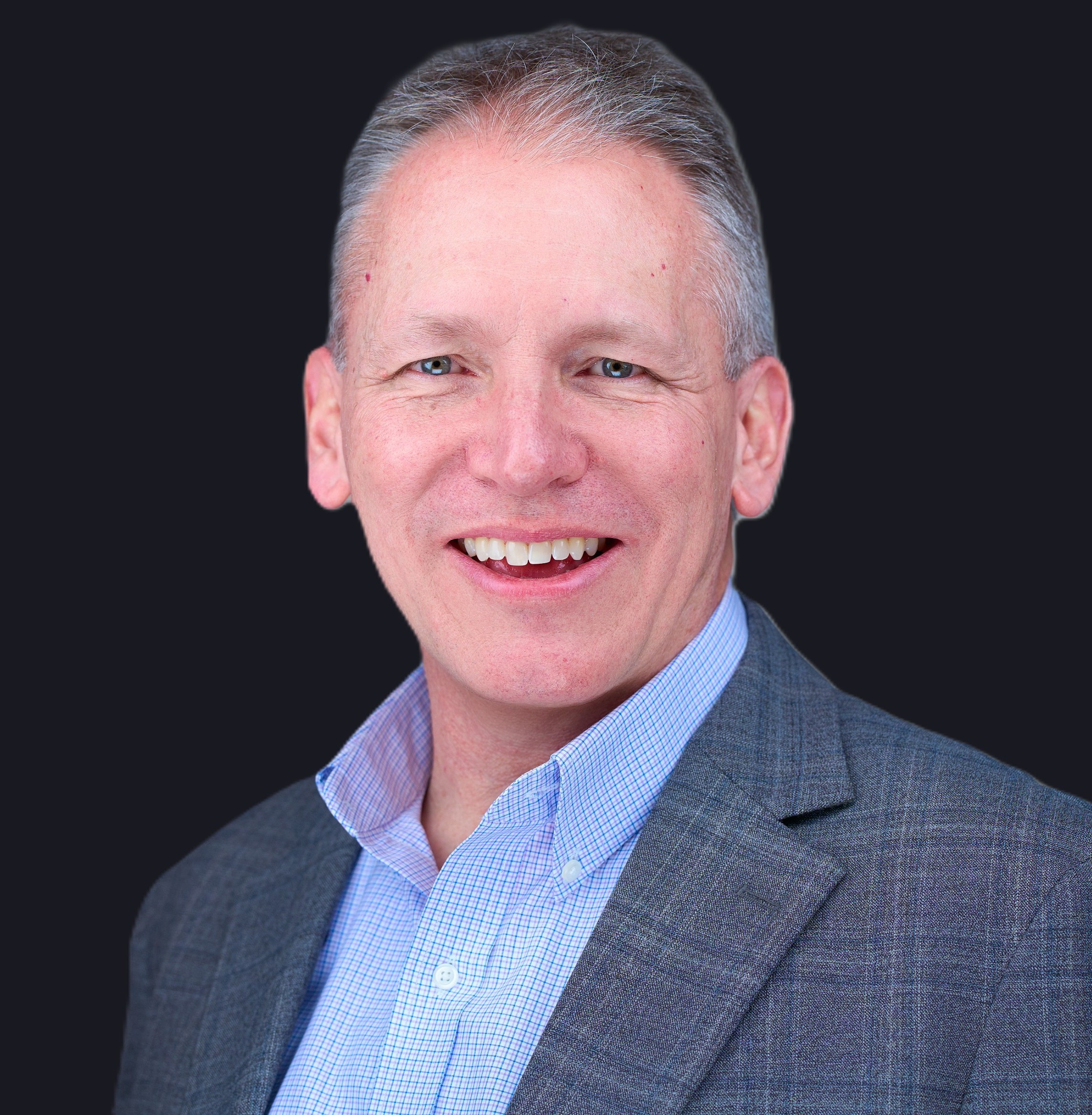 Smiling middle-aged man with short gray hair, wearing a blue dress shirt and a gray plaid suit jacket, posed in front of a dark background.